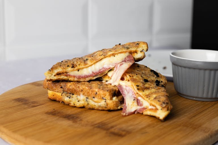 A close-up of a mouthwatering grilled cheese and ham sandwich served on a wooden board, perfect for a hearty breakfast.