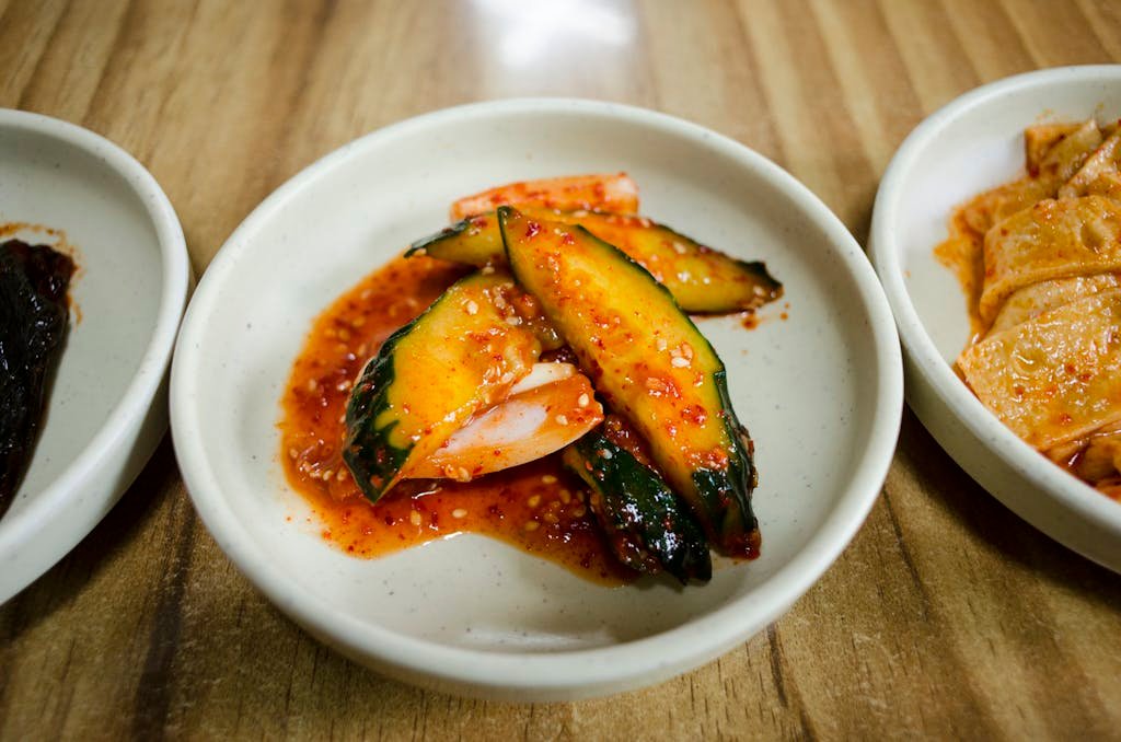 A close-up of spicy Korean cucumber kimchi arranged in a white ceramic bowl on a wooden table.