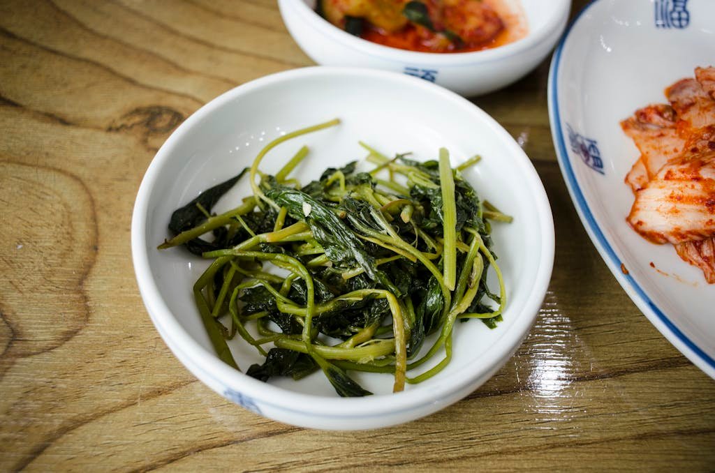 A close-up view of Korean green side dishes in a bowl on a wooden table, featuring vegetables.