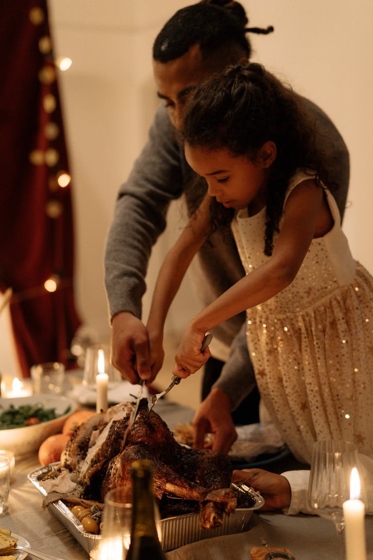 A father and daughter sharing a festive moment carving a turkey together at a holiday meal.