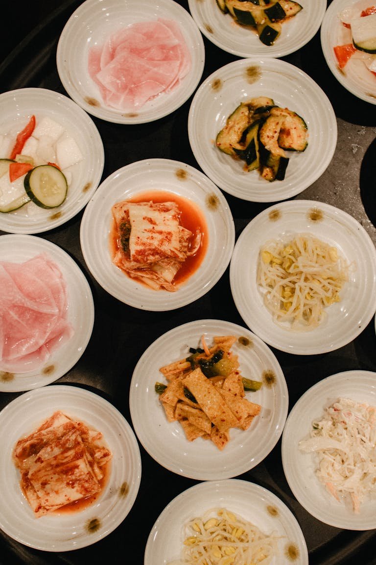 An overhead view of various Korean side dishes served in white bowls.