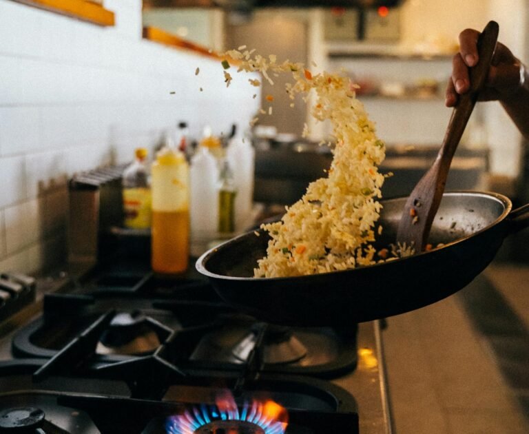 Chef skillfully tossing fried rice in a hot wok over a stove flame in a restaurant kitchen.