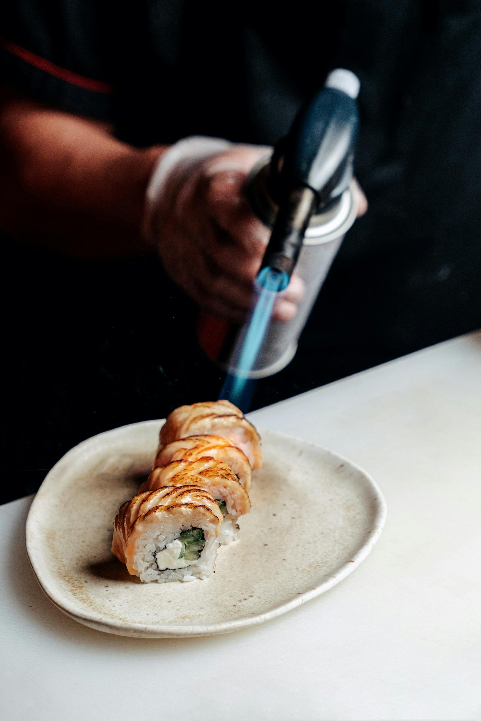 Chef using a culinary torch to sear sushi rolls, highlighting delicious Japanese cuisine preparation.
