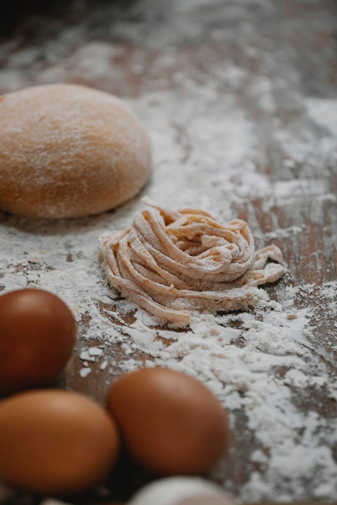 Close-up of fresh homemade pasta dough and eggs on a floured wooden surface.