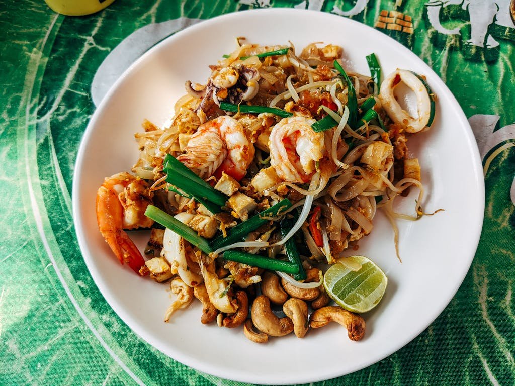 Close-up of a must try street food of Pad Thai with shrimp, vegetables, and lime served on a ceramic plate in Bangkok.