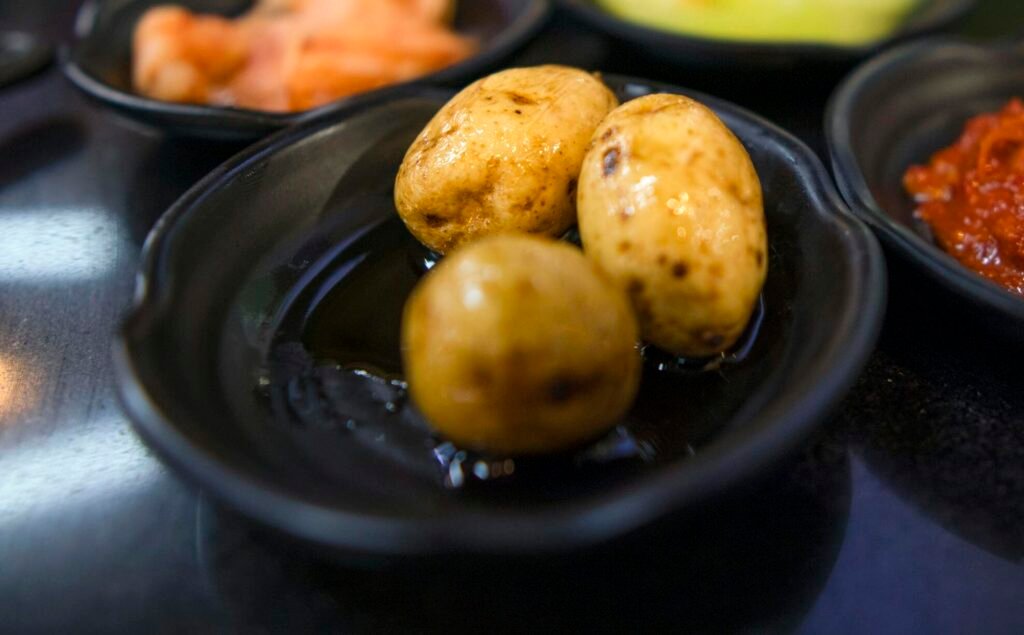A close shot of Korean side dishes including baby potatoes and kimchi on a table.