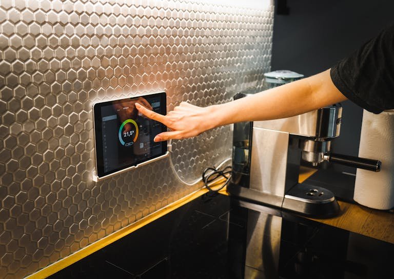 Modern kitchen scene featuring a hand using a tablet to control a smart home system.