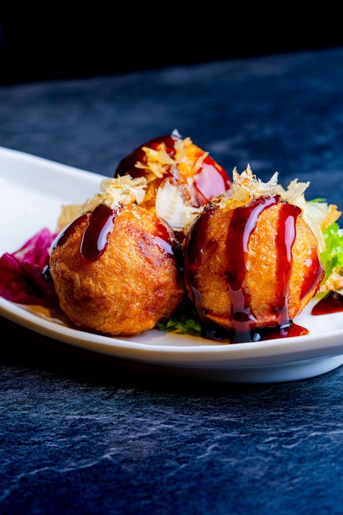 Mouthwatering japanese street food of takoyaki topped with sauce and garnish served on a stylish plate.