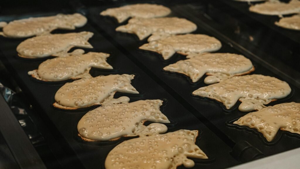 Rows of authentic Japanese stret food of taiyaki pancakes cooking on a grill, showcasing the intricate patterns of the molds.