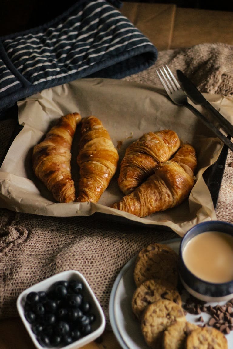 Warm morning setup with croissants, cookies, and coffee for a relaxing breakfast.
