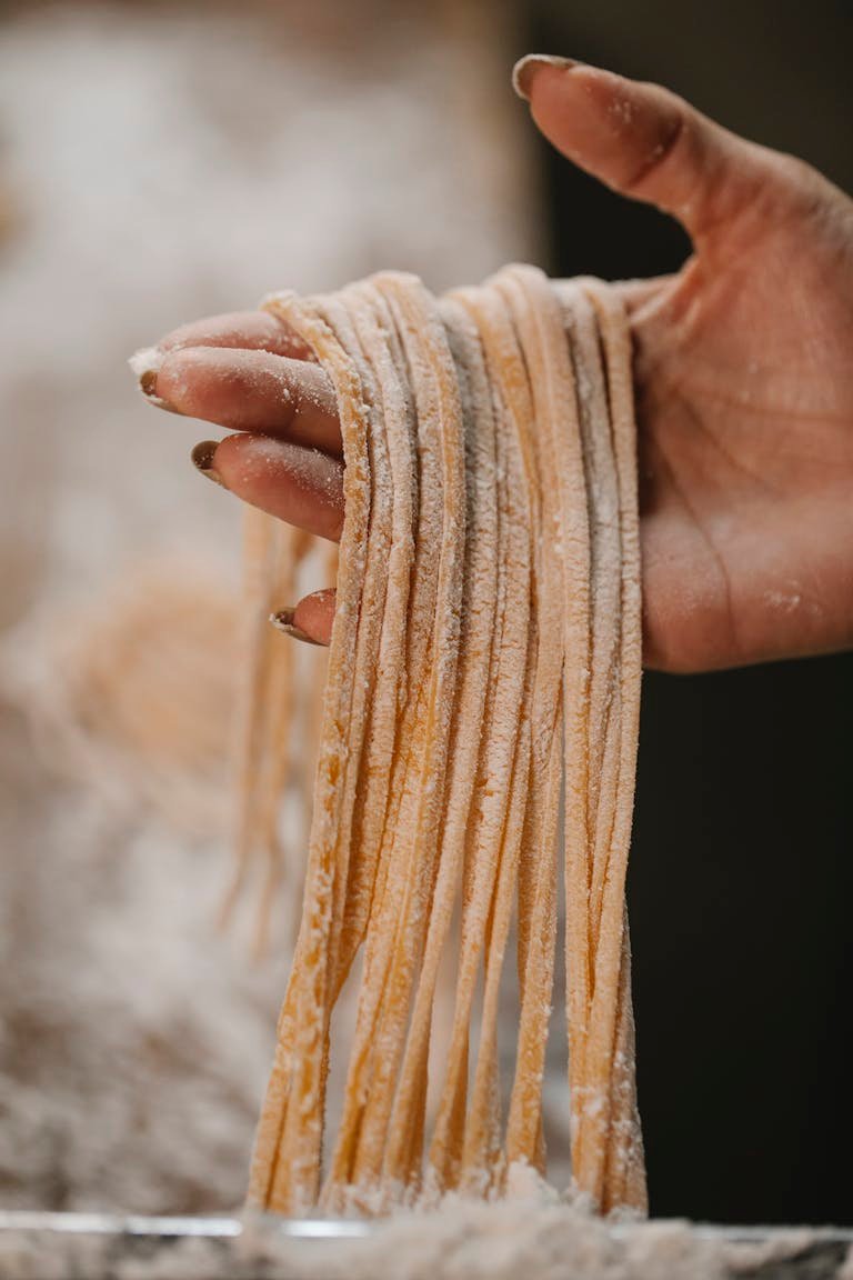 A close-up view of a hand holding freshly made authentic italian pasta strings, dusted with flour.
