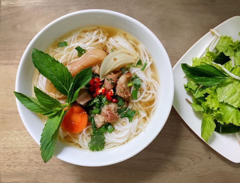 A fresh and vibrant bowl of Vietnamese Pho noodle soup with herbs and vegetables.
