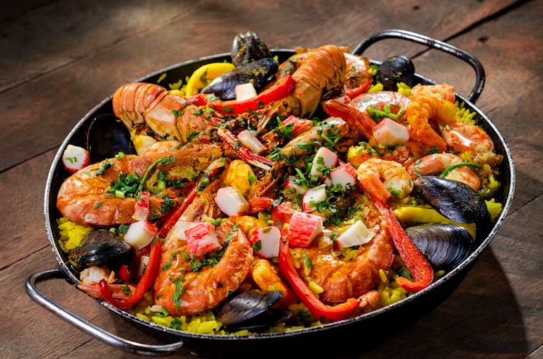 A paella pan showing colorful seafood with shrimp, mussels, and rice in a traditional paella pan.