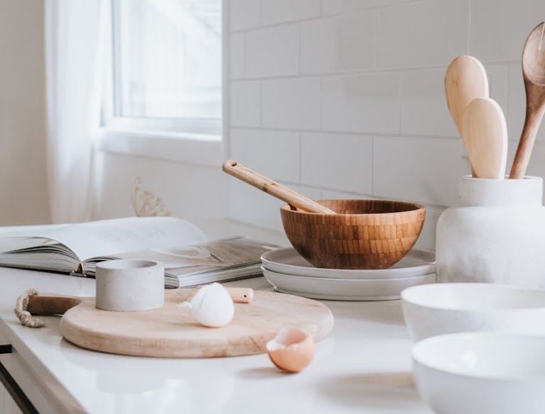 A serene minimalist kitchen setup featuring wooden bowls, spoons, and ceramic ware on a marble surface.
