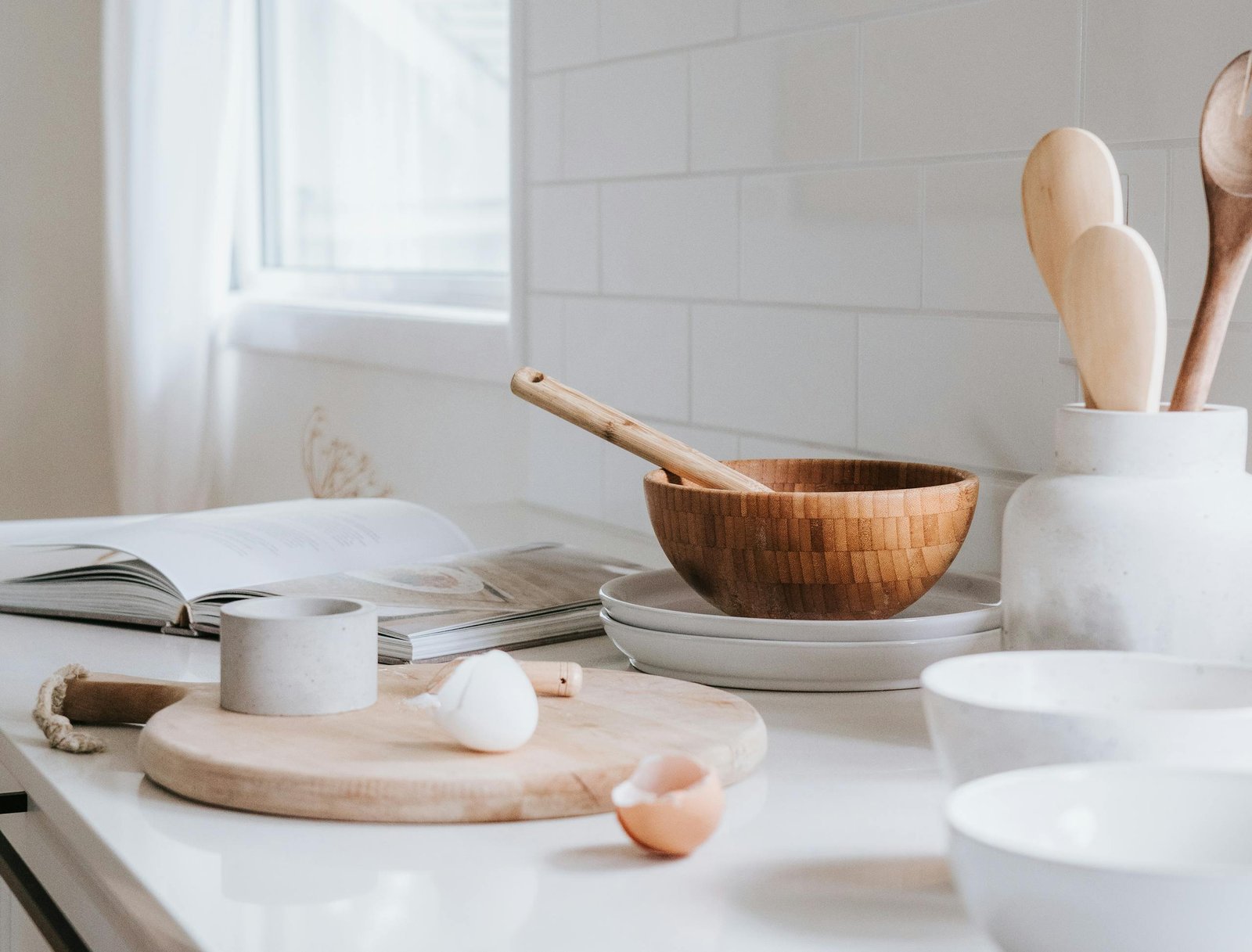 A serene minimalist kitchen setup featuring wooden bowls, spoons, and ceramic ware on a marble surface.