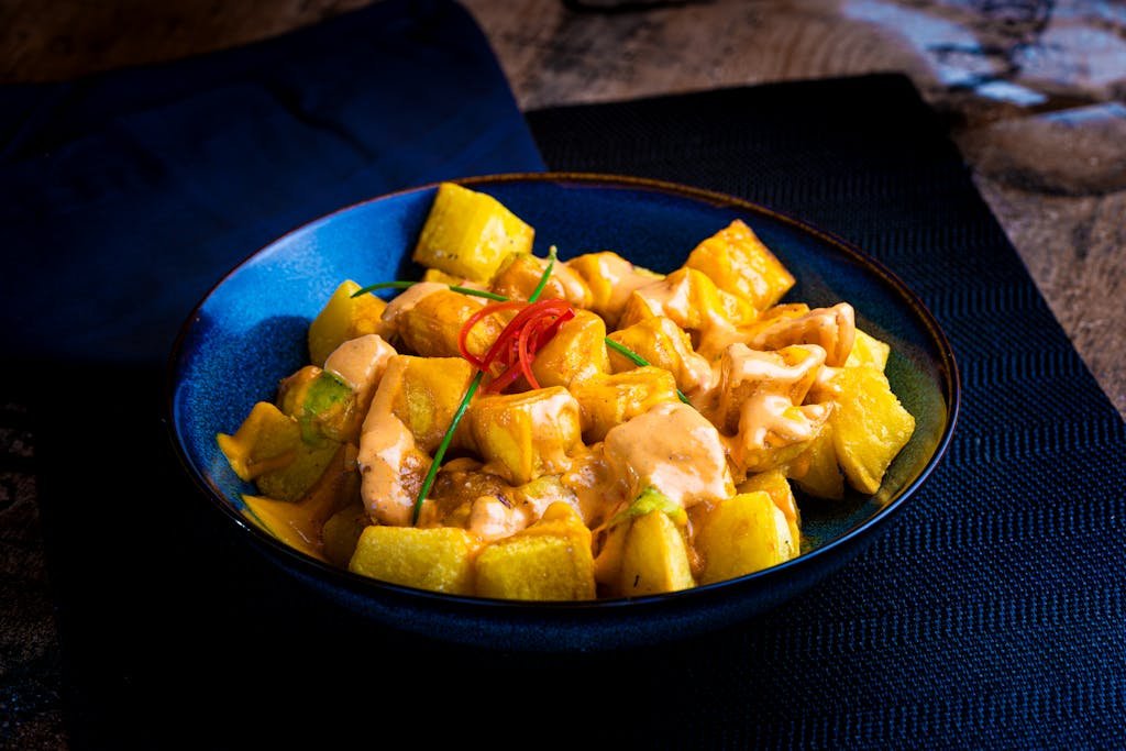 A vibrant spanish tapas recipes showcasing a dish of patatas bravas with rich sauce on a blue plate, perfect for culinary enthusiasts.