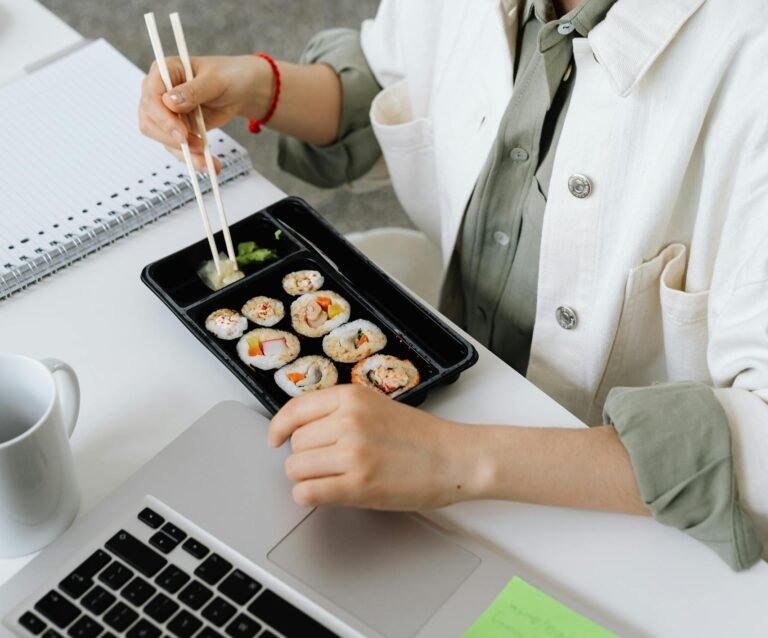 A woman enjoying a bento box with sushi during a work break at her office desk with a laptop.