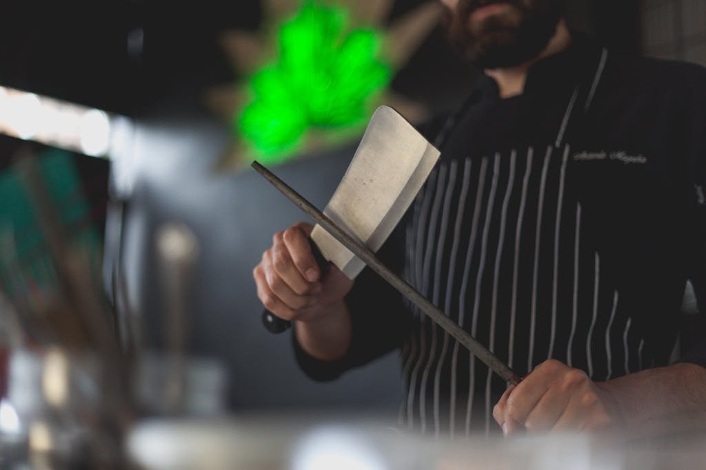 Close-up of a chef using a knife sharpening system to sharpen a kitchen knife with a honing steel in a professional kitchen setting.