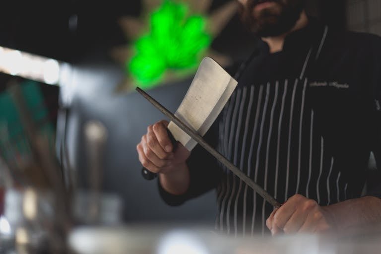 Close-up of a chef sharpening a kitchen knife with a honing steel in a professional kitchen setting.