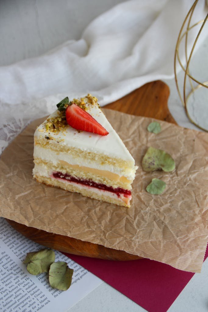 Delicious slice of my Victoria sponge cake recipe 2.0 with a strawberry jam layer on parchment, perfect for dessert time.