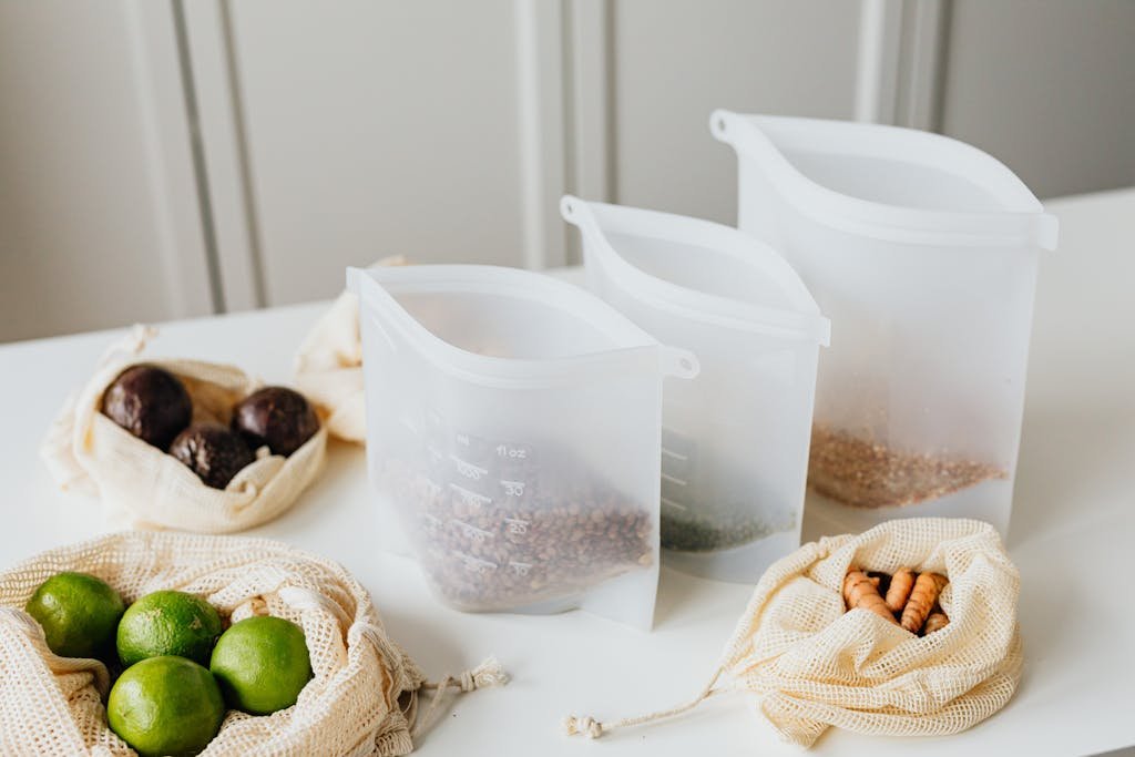 Divided silicone food storage bags showing reusable silicone and cloth bags storing lime, turmeric, and grains on a kitchen table.