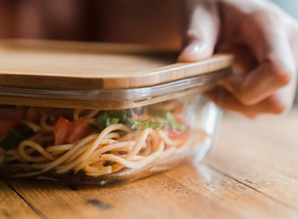 Hand placing lid on a container of noodles, highlighting food storage solutions.