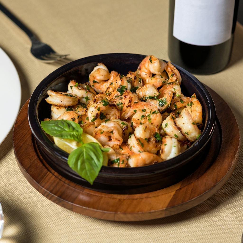 Spanish tapas recipes of Sizzling garlic herb shrimp in a ceramic dish, garnished with basil and lemon, ready to serve.