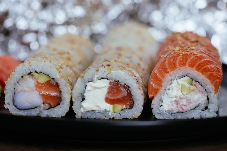 Sushi Making for Beginners - Showing Tempting close-up of assorted sushi rolls with salmon and cream cheese on a black plate.