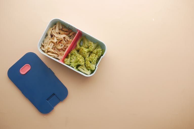 Top view of a divided food storage container with broccoli and noodles, perfect for a healthy meal.