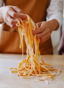A person carefully handling freshly cut uncooked pasta strands in a kitchen setting.