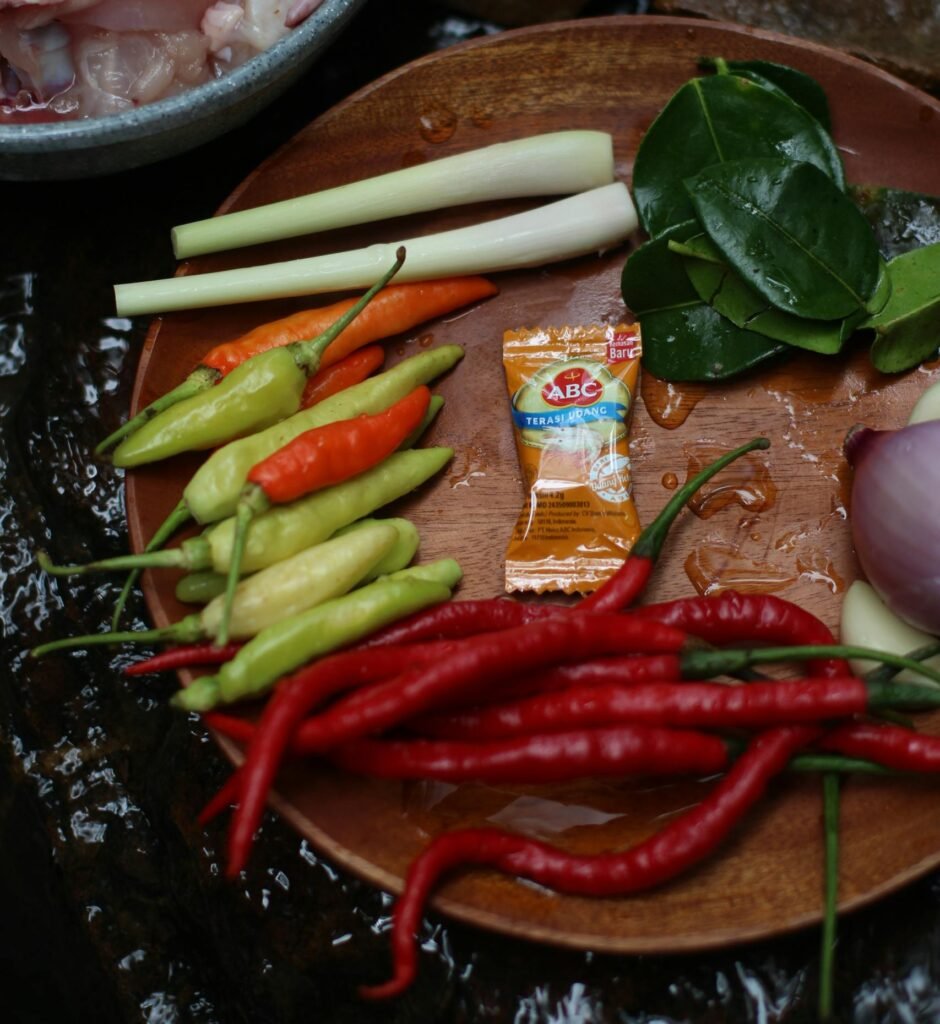 A selection of fresh ingredients for Asian cooking, featuring chili peppers, lime leaves, and lemongrass.