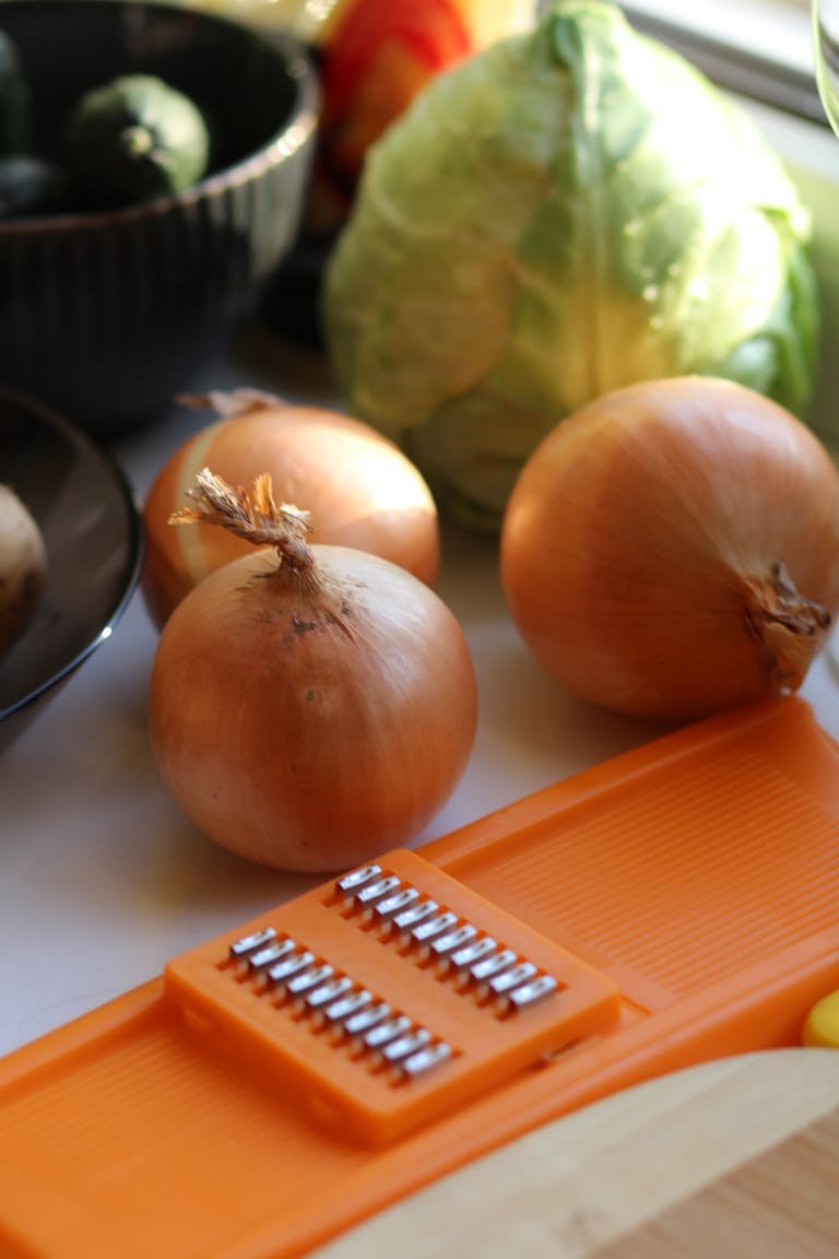 A vibrant close-up of onions and cabbage with a mandoline slicer on a sunny kitchen counter.