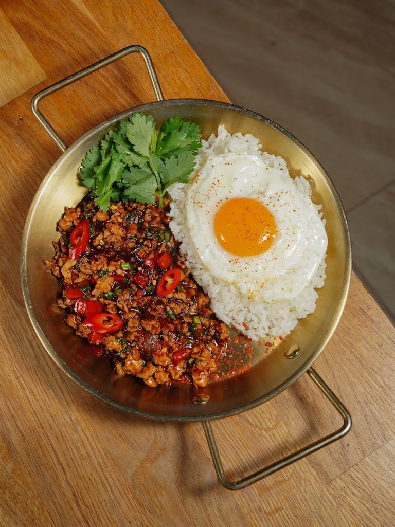 Appetizing Thai ingredients such as basil chicken served with rice and a perfectly cooked fried egg.