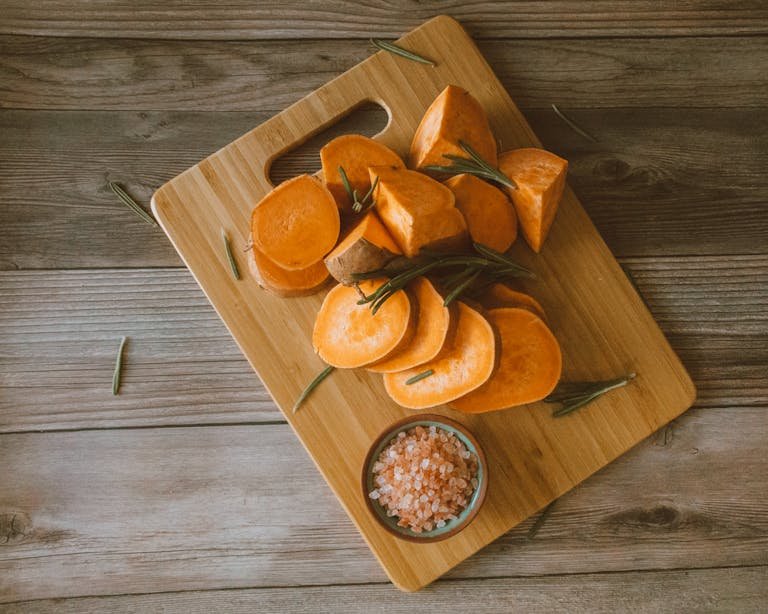 Chopped sweet potatoes on a organic bamboo boards with Himalayan salt and rosemary, perfect for rustic food themes.