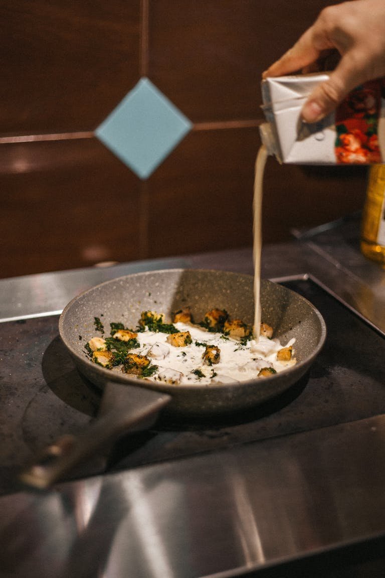 Close-up of cream being poured into a hot frying pan with vegetables displaying a nice eco-friendly cookware.