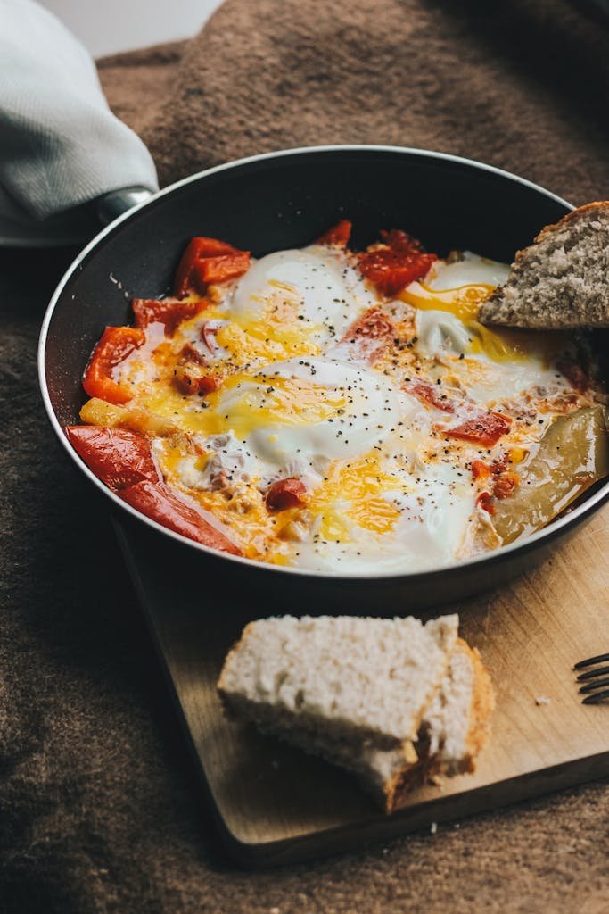 Close-up of homemade shakshuka with tomatoes and eggs cooked in a non-stick pan with bread on the side.