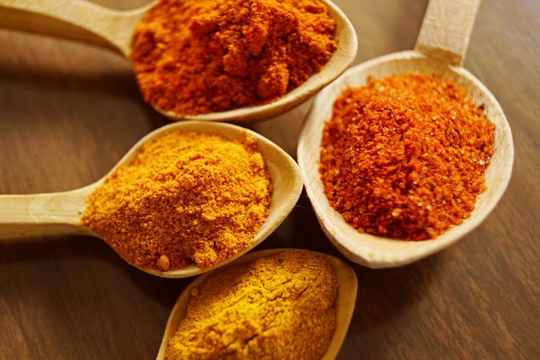 Close-up of vibrant spices for Indian curries like turmeric and chili powder in wooden spoons.
