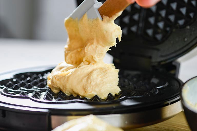 Delicious waffle batter being spread on a the best mini waffle maker for a tasty breakfast.