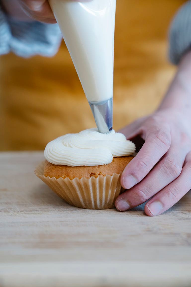 Part of our cake decorating sets of a hand piping whipped cream onto a cupcake, showcasing food artistry.