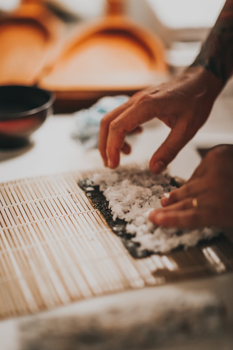 Close-up of hands preparing sushi using a sushi making kit featuring bamboo mat, showcasing culinary skills.