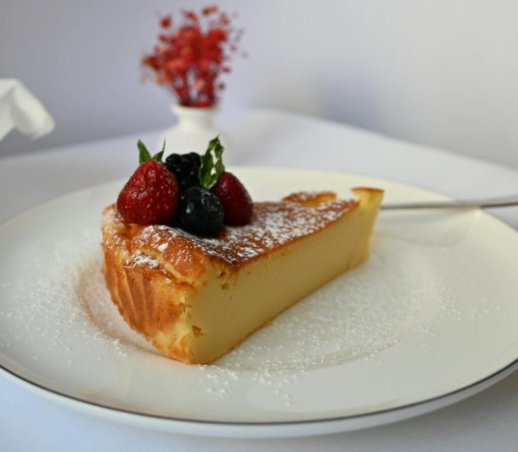 Delicious gourmet cheese cake slice topped with fresh berries and powdered sugar.