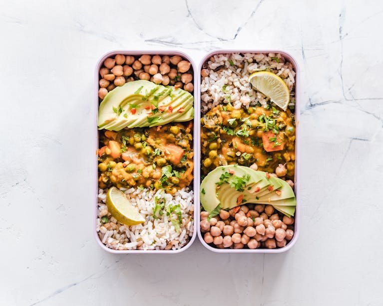 Delicious meal prep hacks in lunchboxes featuring chickpeas, rice, avocado, and curry on a white background.