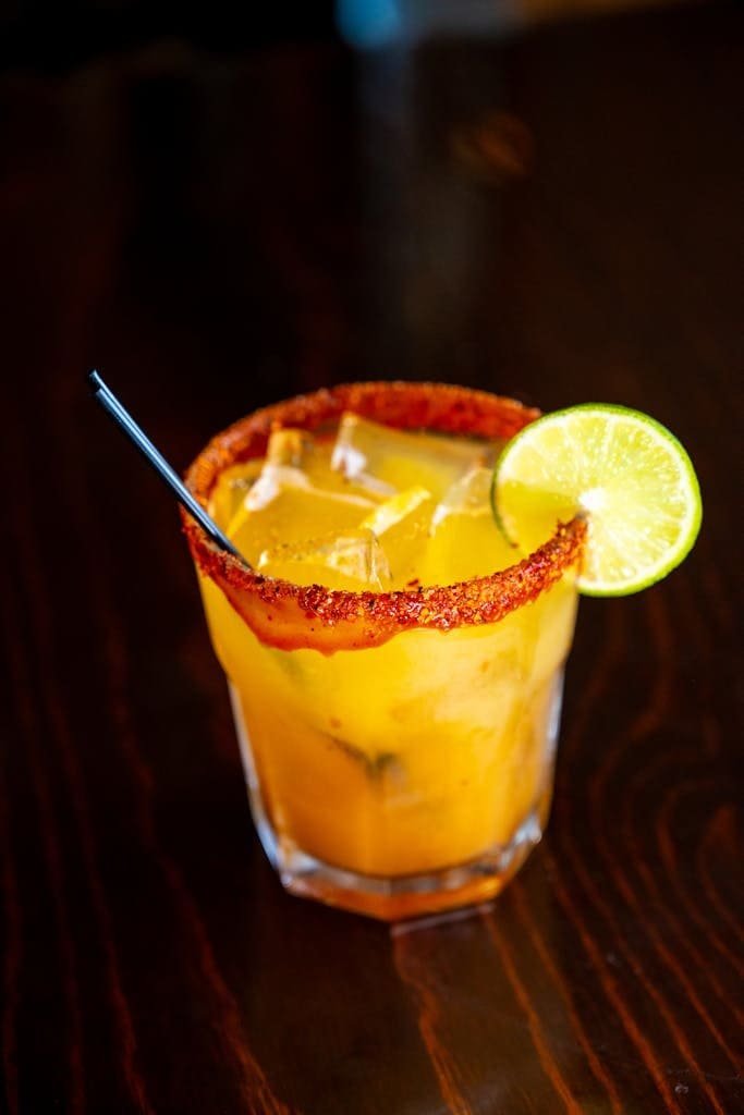 Vibrant citrus cocktail with a lime slice and chili rim in a clear glass on a dark background.