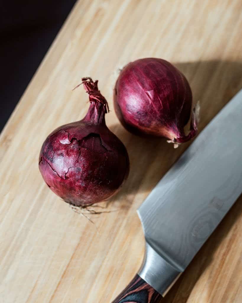 Close-up of fresh red onions on a wooden board with a chef's knife.