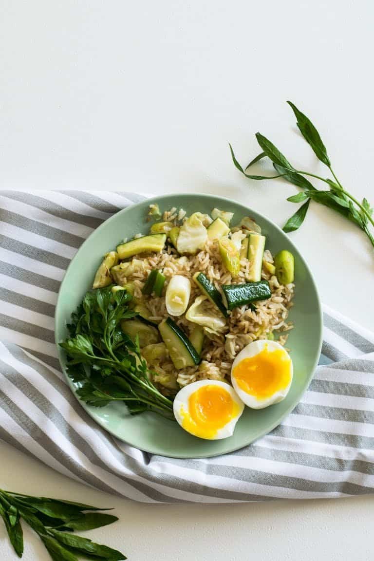 A top view of a 15-minute healthy dinner with a vegetable rice dish with soft-boiled eggs on a light green plate.
