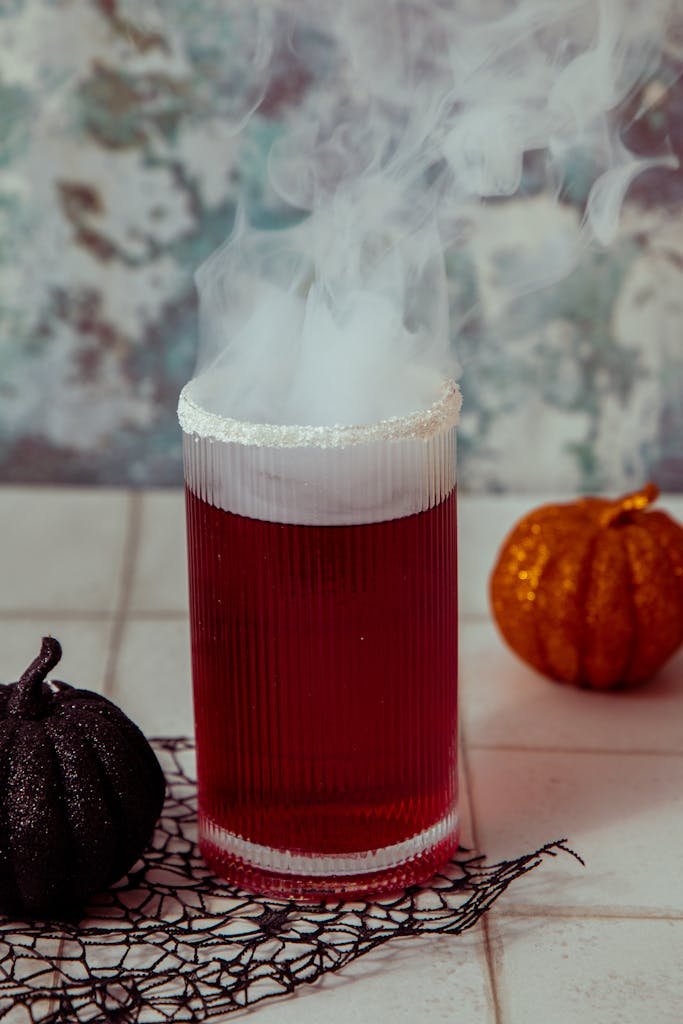 A steaming red cocktail in a glass, perfect for Halloween with decorative pumpkins.