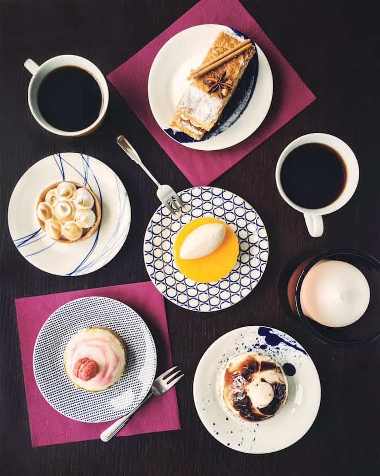 An artistic flat lay of assorted pastries and coffee cups on a dark table setting, perfect for brunch imagery.