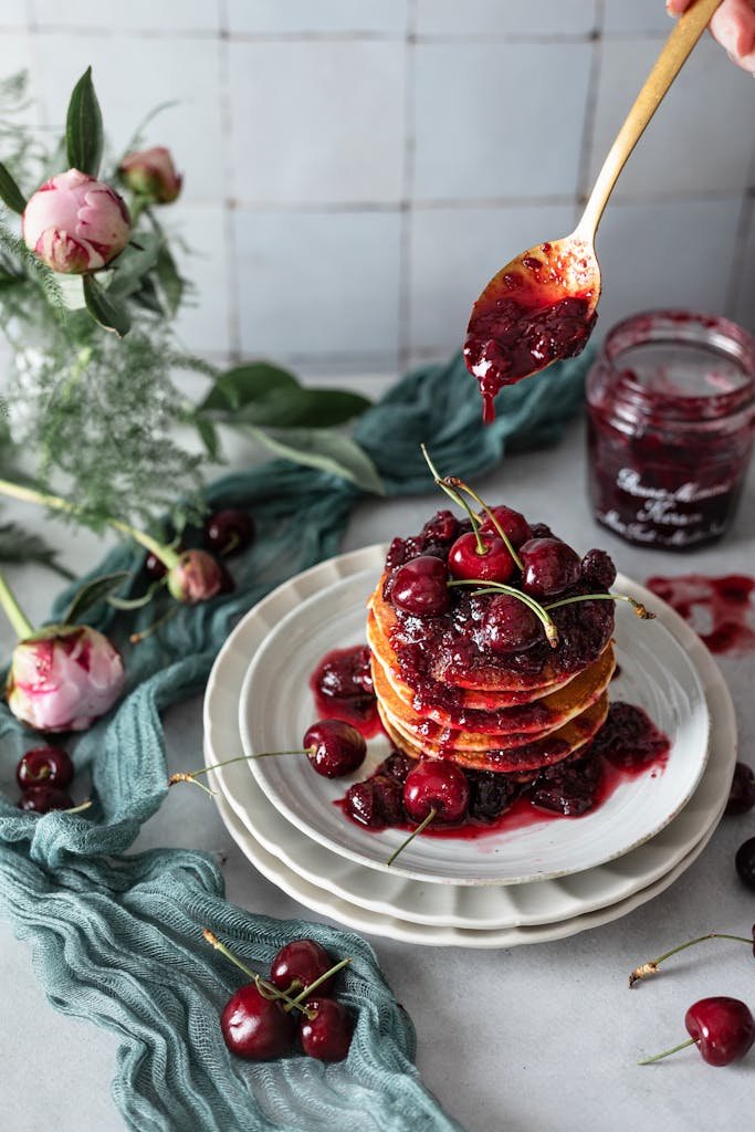 Delicious pancakes topped with cherries and jam, perfect brunch setup with a rustic feel.