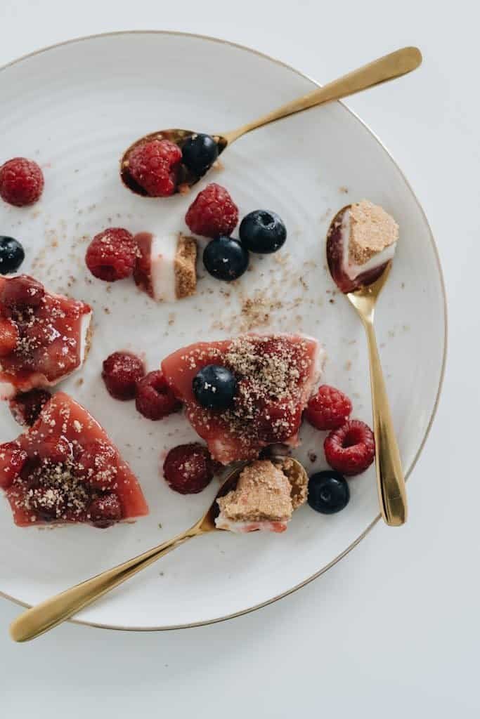 Tasty berry cheesecake dessert with raspberries and blueberries served elegantly with gold spoons.