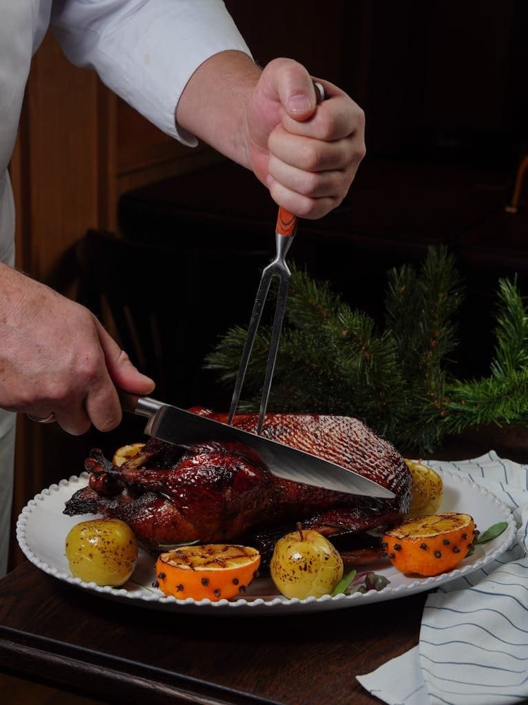 A chef carves a succulent roasted duck garnished with oranges and apples, evoking a festive mood.